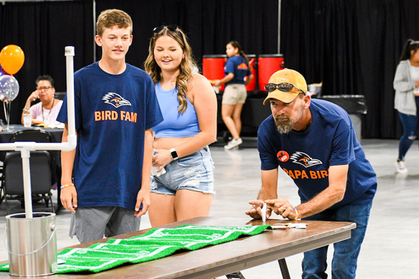A man flicking a paper football through a mini goal post while students look on